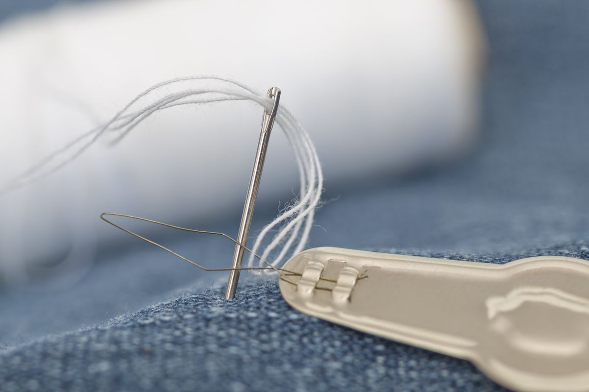 A threaded needle ready for a repair to denim