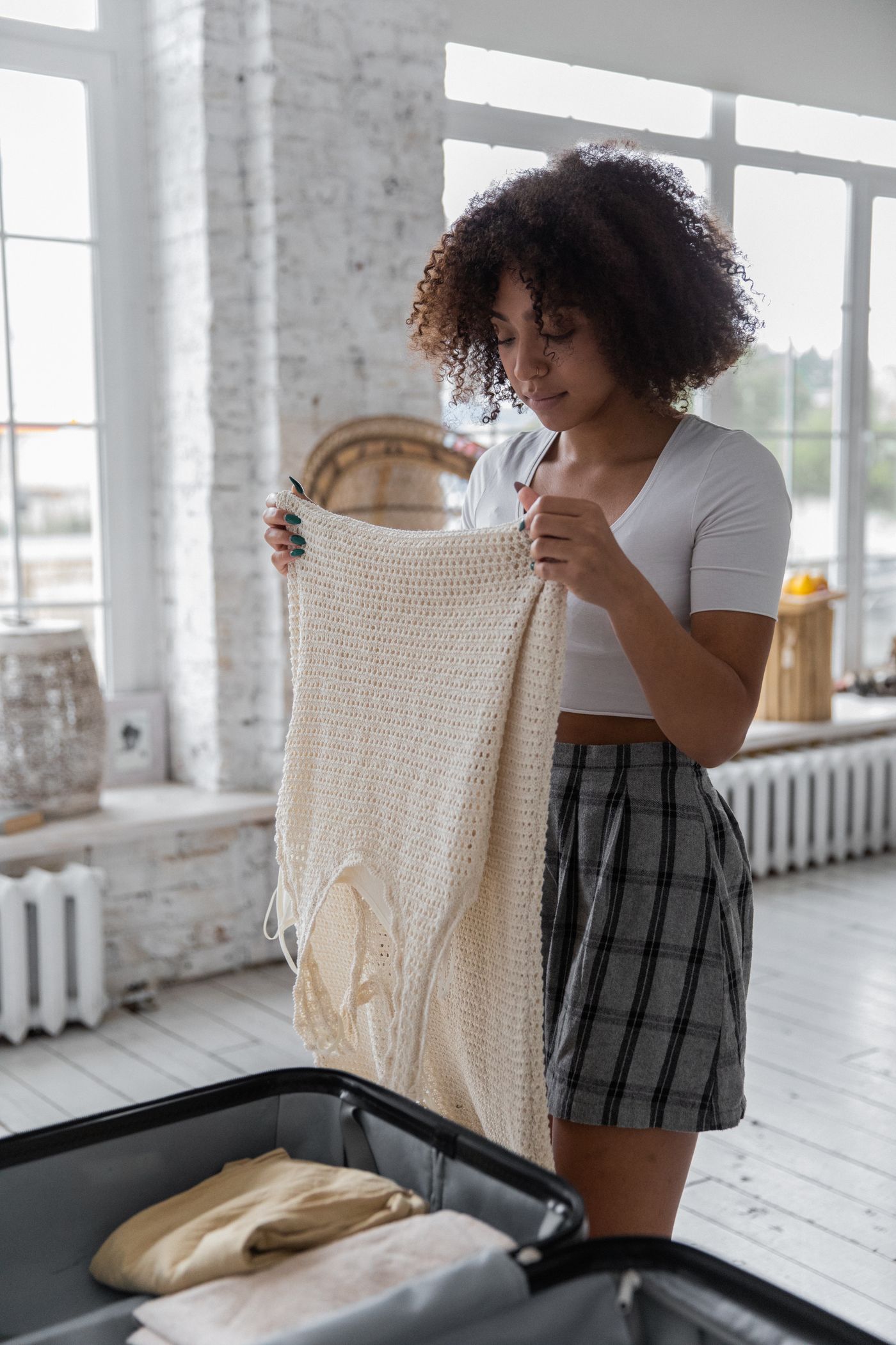 A woman examining a garment beside an open suitcase