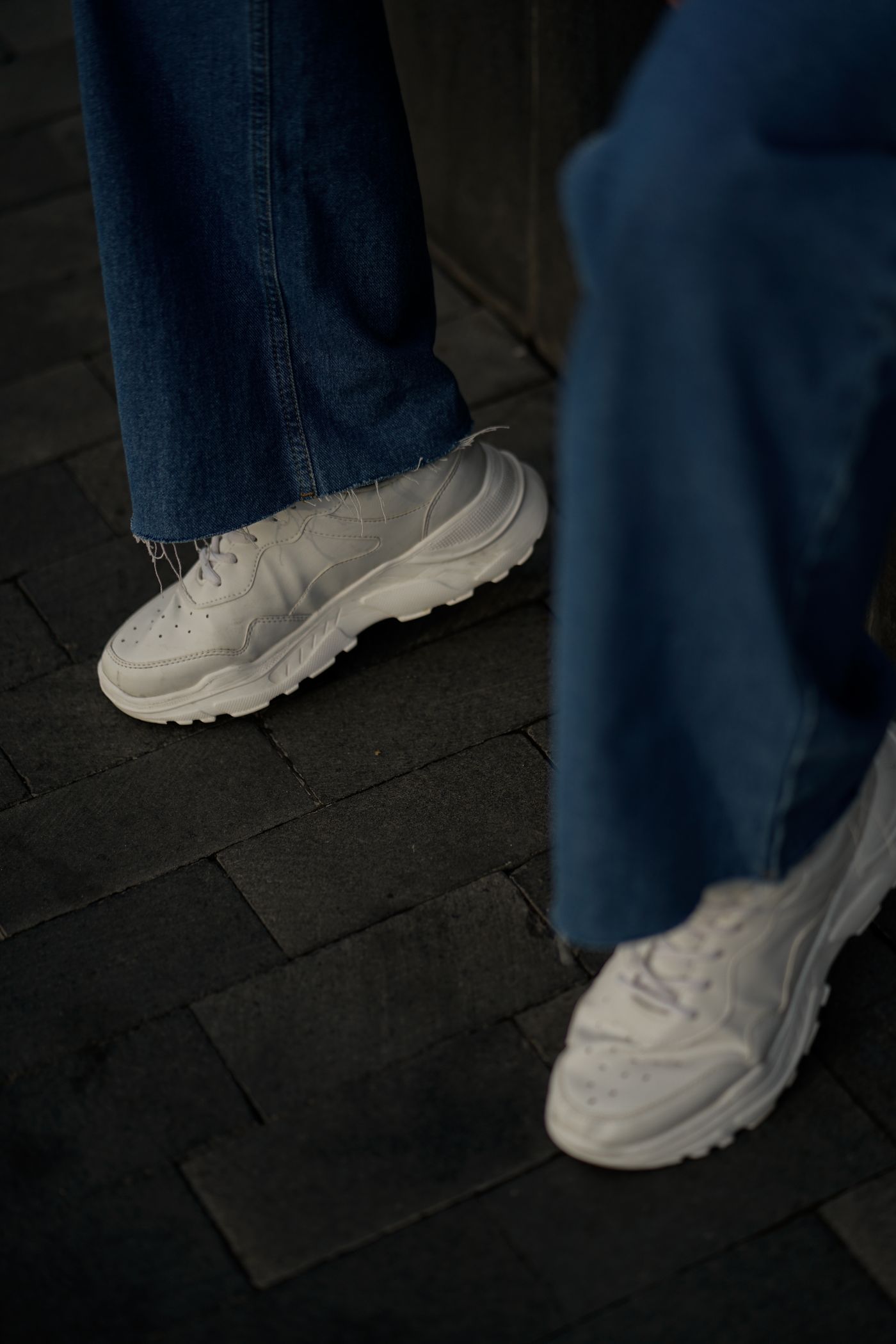 White trainers beneath wide denim trouser hems