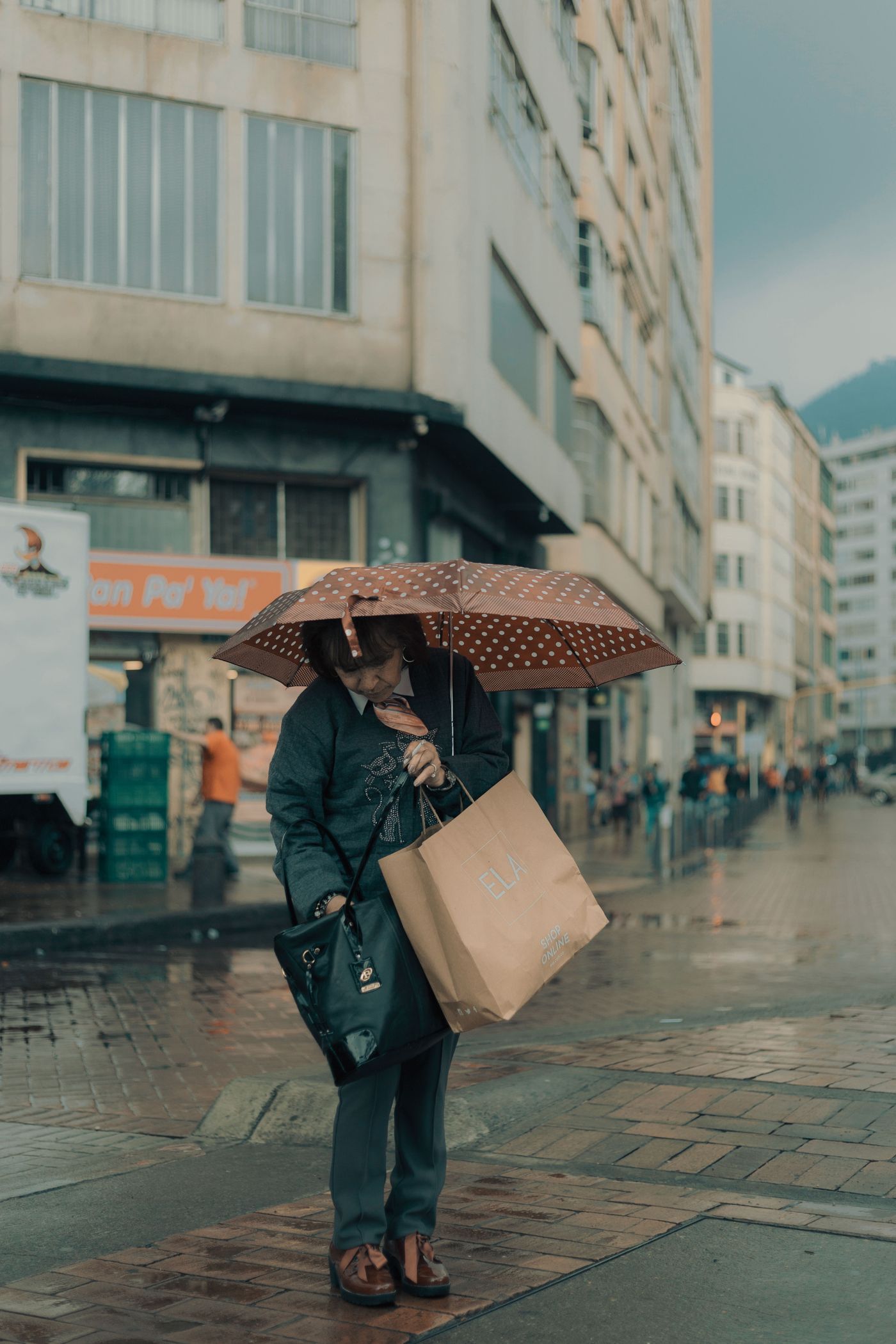 A woman carrying a tote bag beneath an umbrella