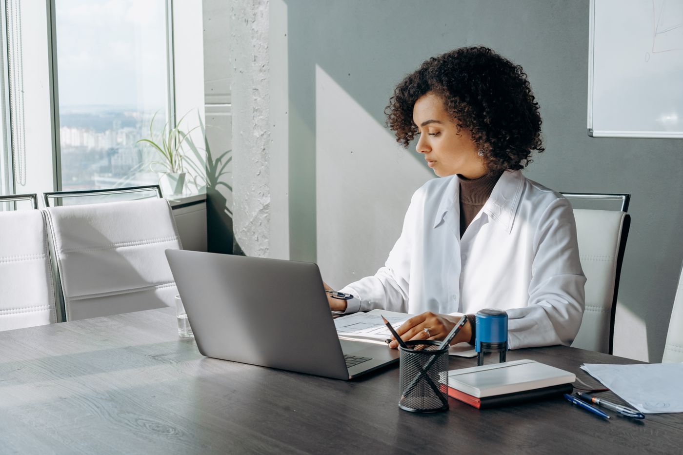 A woman wearing a light blazer at a sunlit desk